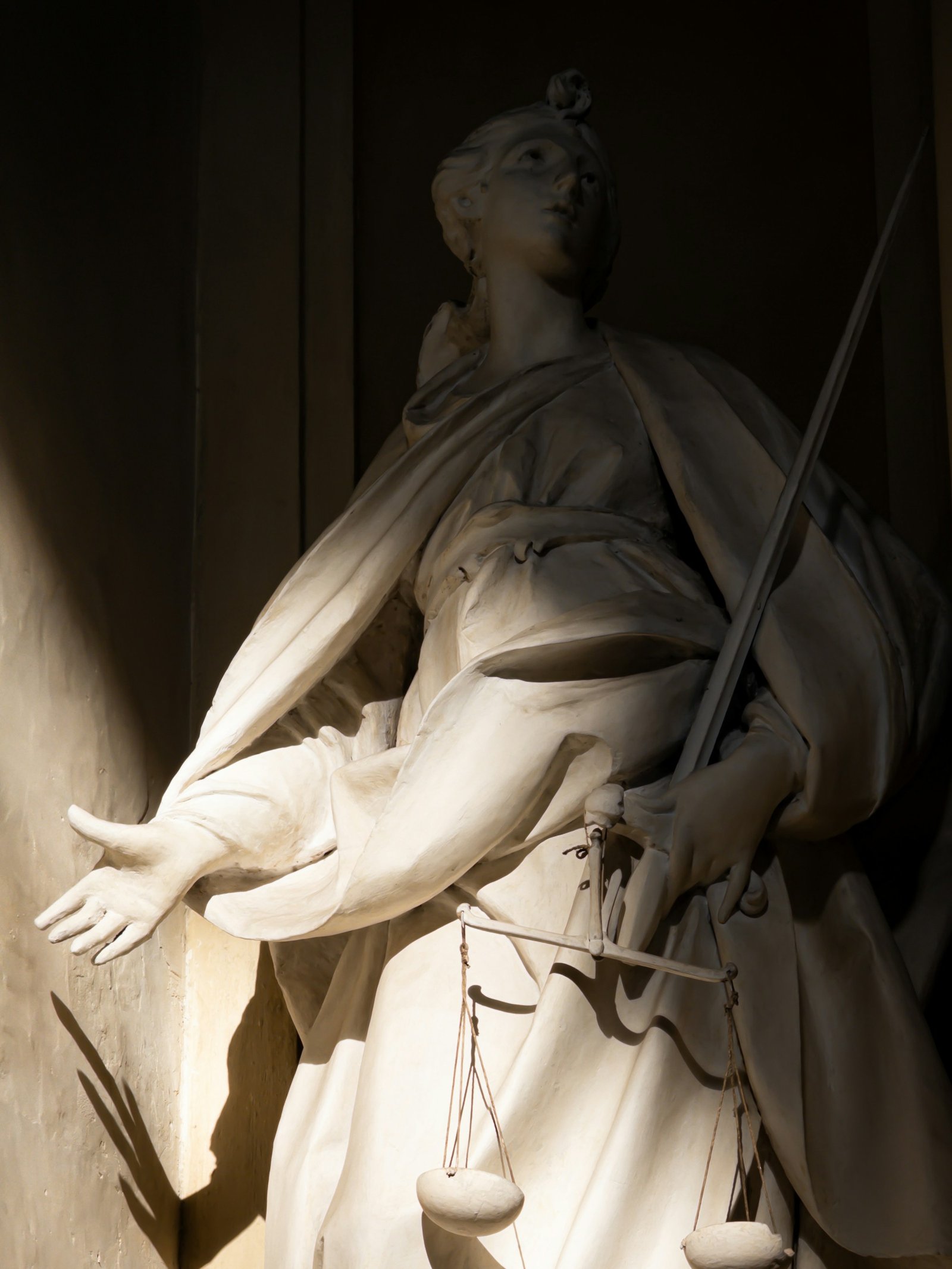 A marble figure of Justice holding a sword and a set of scales, lit against a dark interior.