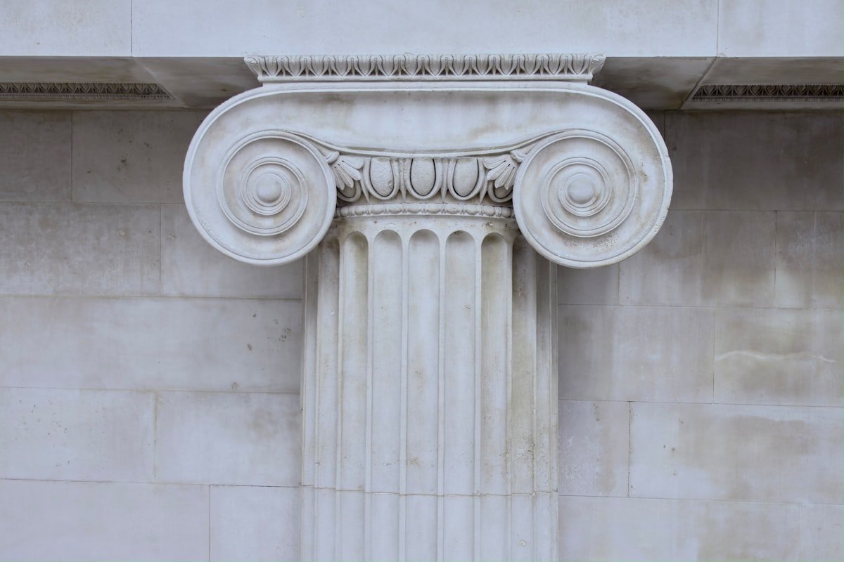 Carved detail of an Ionic column capital in pale stone.