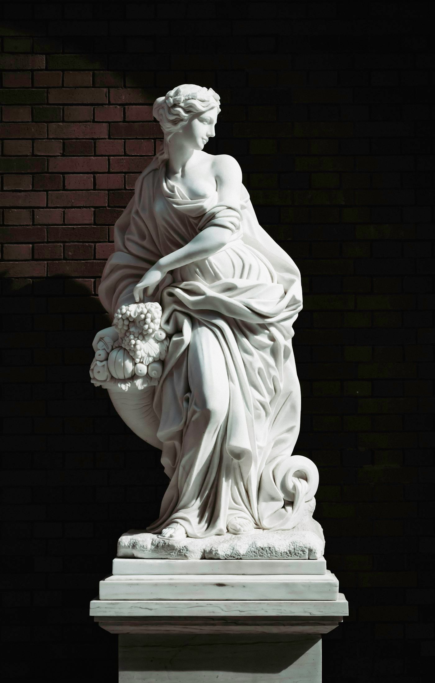 A white marble sculpture of a robed figure against a dark wall.